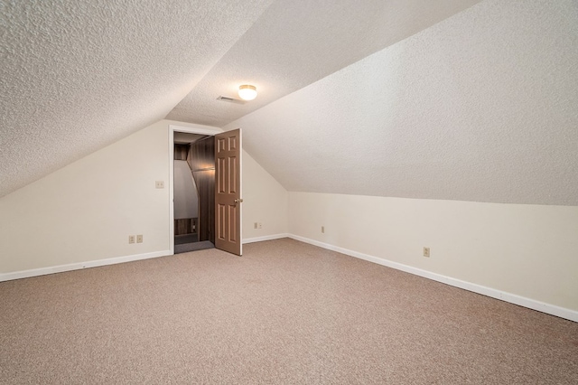 additional living space featuring visible vents, baseboards, lofted ceiling, a textured ceiling, and carpet floors