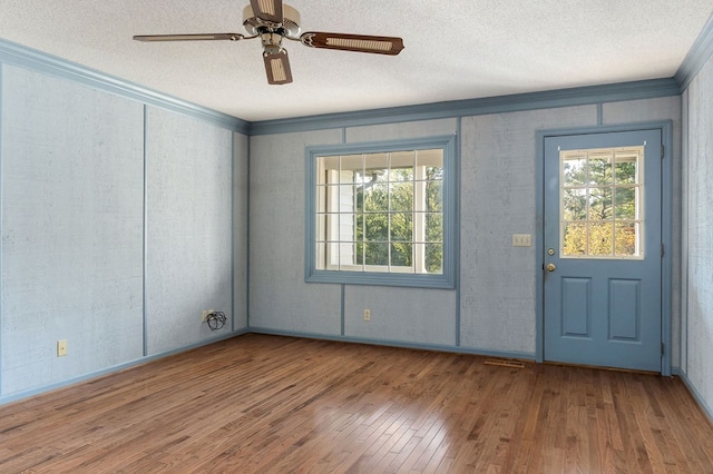 unfurnished room with a healthy amount of sunlight, a textured ceiling, ornamental molding, and wood finished floors