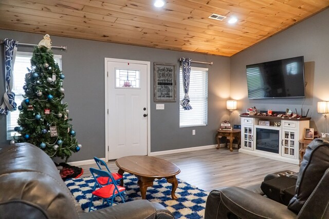 living area with lofted ceiling, light wood finished floors, wooden ceiling, and a glass covered fireplace