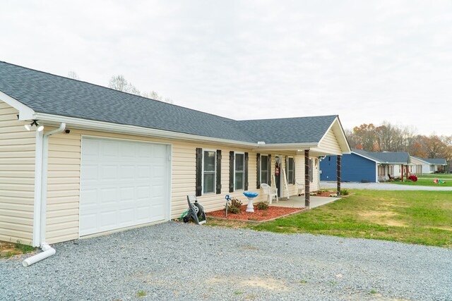 ranch-style home featuring a garage, a shingled roof, gravel driveway, a front lawn, and a porch