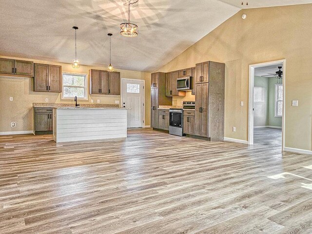 kitchen featuring pendant lighting, brown cabinets, light wood finished floors, appliances with stainless steel finishes, and high vaulted ceiling