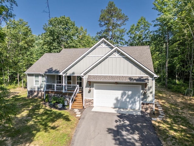 view of front facade with roof with shingles, covered porch, an attached garage, driveway, and a front lawn