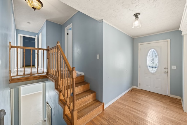 entrance foyer featuring light wood-style flooring, ornamental molding, a textured ceiling, stairway, and baseboards