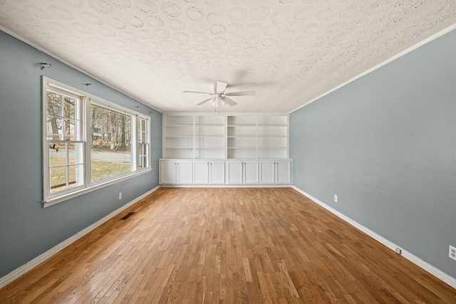 unfurnished room featuring built in shelves, a textured ceiling, wood finished floors, baseboards, and ceiling fan