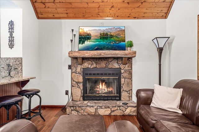 living room with wood ceiling, lofted ceiling, a stone fireplace, and wood finished floors