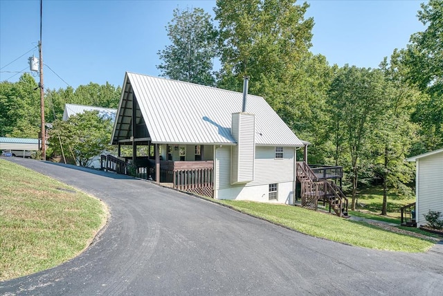 exterior space featuring aphalt driveway, stairs, a front lawn, and metal roof