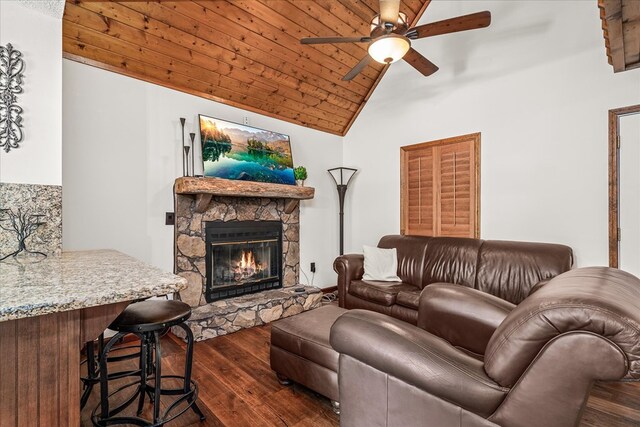 living room featuring ceiling fan, wood ceiling, lofted ceiling, a stone fireplace, and wood finished floors