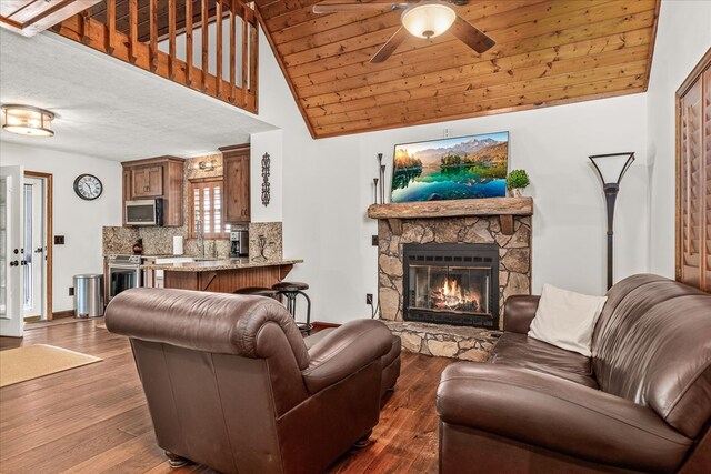 living area featuring dark wood-style floors, baseboards, a stone fireplace, vaulted ceiling, and wood ceiling