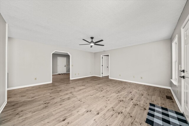 unfurnished living room featuring arched walkways, baseboards, and light wood-style floors