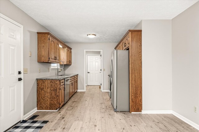 kitchen with appliances with stainless steel finishes, brown cabinetry, a textured ceiling, light wood-type flooring, and baseboards