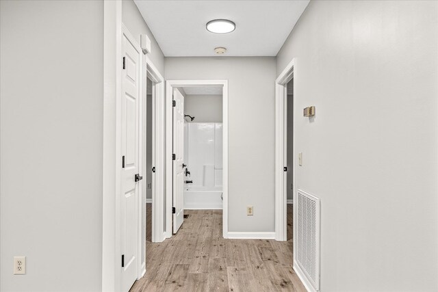 corridor with light wood-style floors, baseboards, and visible vents