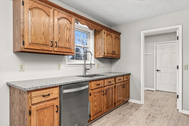 kitchen with light wood finished floors, stainless steel dishwasher, brown cabinetry, a sink, and baseboards