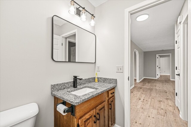 half bathroom with toilet, baseboards, wood finished floors, and vanity