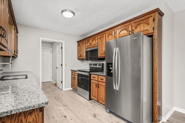 kitchen with brown cabinets, stainless steel appliances, light wood-style floors, light stone countertops, and baseboards