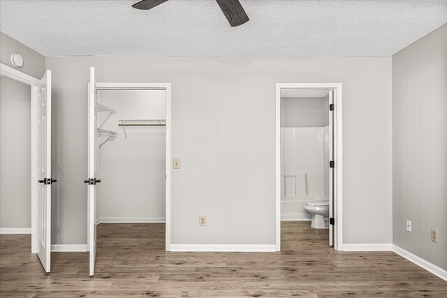 unfurnished bedroom featuring wood finished floors, ensuite bathroom, a walk in closet, a textured ceiling, and a closet