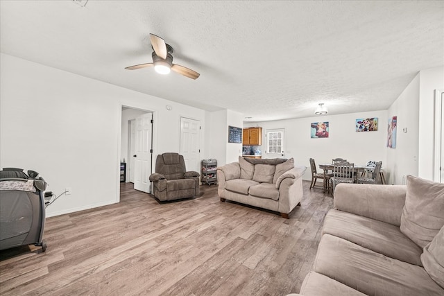 living area with a ceiling fan, baseboards, light wood-style flooring, and a textured ceiling