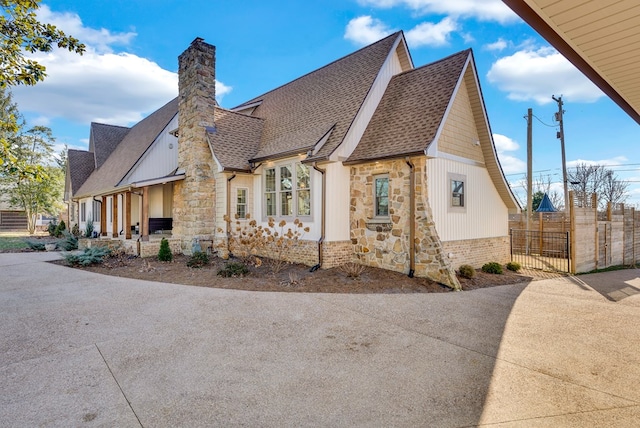 view of home's exterior featuring stone siding, a shingled roof, a chimney, and fence