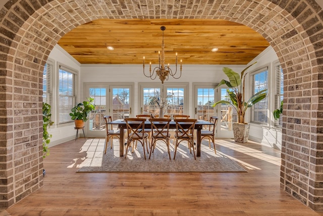 dining space featuring light wood-type flooring, an inviting chandelier, arched walkways, and wooden ceiling