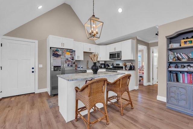 kitchen featuring appliances with stainless steel finishes, a breakfast bar, hanging light fixtures, light stone countertops, and white cabinetry