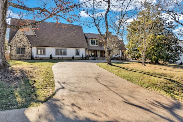 view of front of home with driveway, stone siding, a chimney, and a front lawn