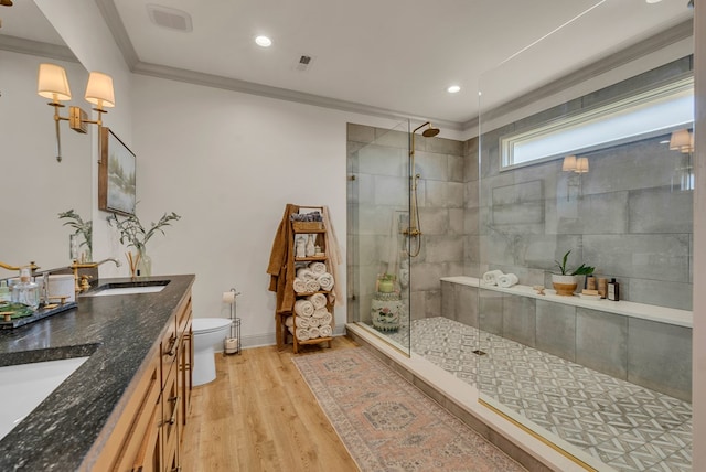 full bathroom with toilet, ornamental molding, a sink, a tile shower, and wood finished floors