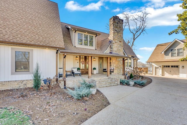 view of front of house featuring a garage, a porch, a chimney, and a shingled roof