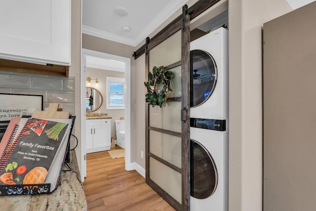 laundry room with crown molding, a barn door, stacked washing maching and dryer, light wood-type flooring, and baseboards