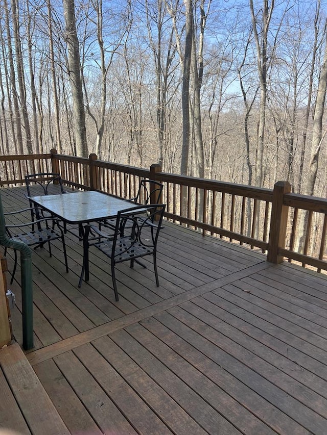 wooden deck featuring outdoor dining space and a view of trees