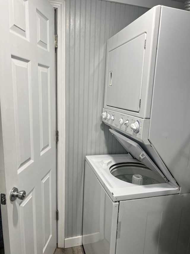 clothes washing area featuring laundry area, wooden walls, and stacked washer and clothes dryer