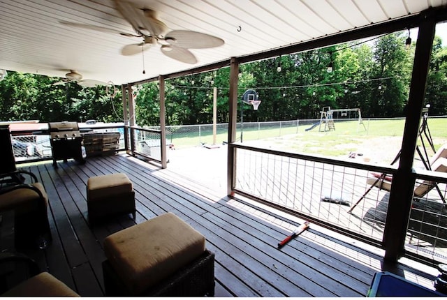 wooden terrace with fence, a ceiling fan, a playground, and a yard