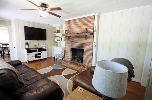 living room featuring built in features, a ceiling fan, dark wood-style floors, crown molding, and a brick fireplace