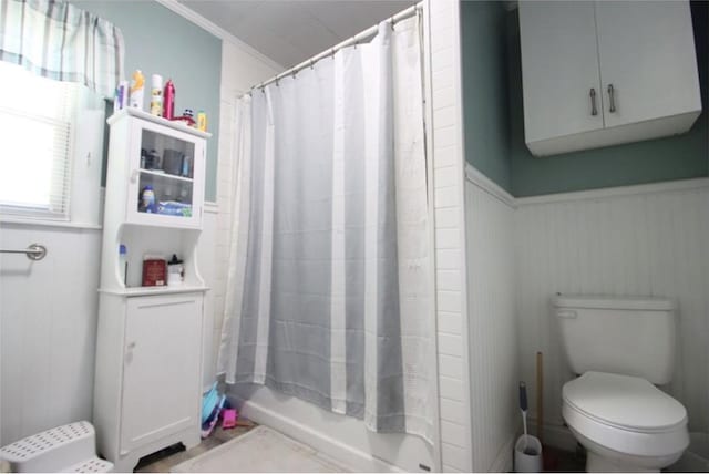 bathroom with toilet, shower / bath combination with curtain, and wainscoting