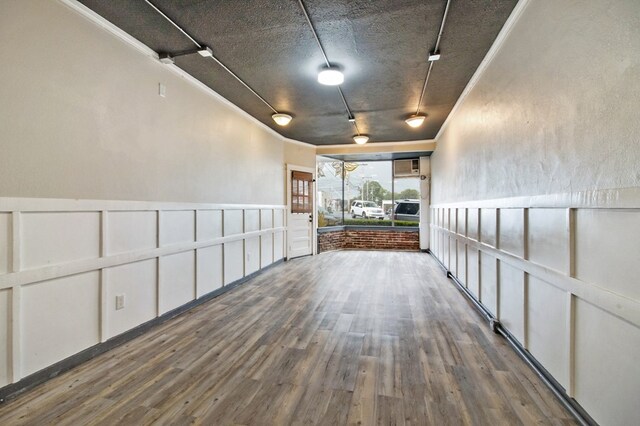 empty room with a wainscoted wall, rail lighting, a decorative wall, dark wood-type flooring, and ornamental molding