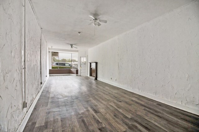 unfurnished living room featuring ceiling fan, a textured wall, baseboards, and wood finished floors