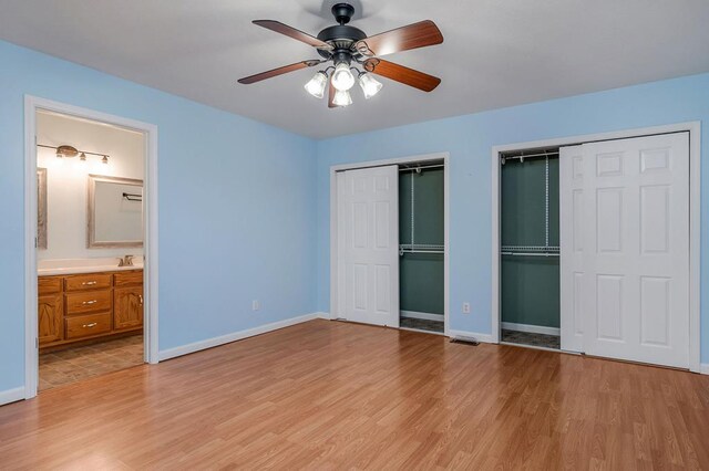 unfurnished bedroom with baseboards, light wood finished floors, and multiple closets