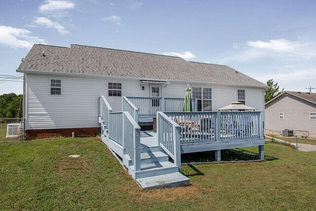 rear view of property with central AC, a lawn, a wooden deck, and roof with shingles