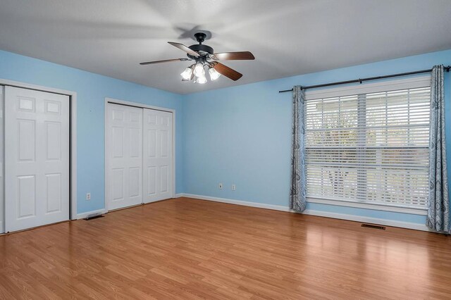 unfurnished bedroom with baseboards, visible vents, ceiling fan, light wood-type flooring, and two closets