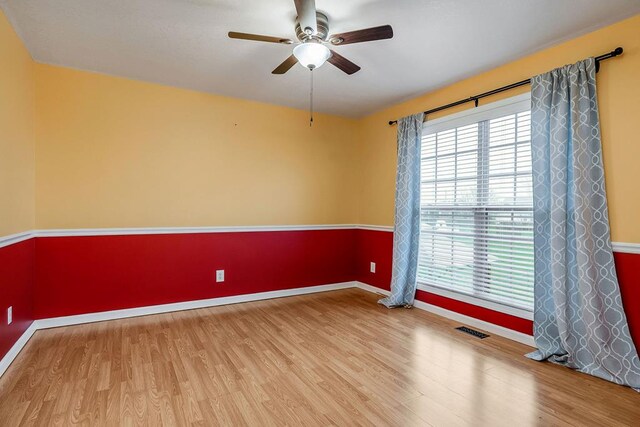 spare room featuring a ceiling fan, visible vents, baseboards, and wood finished floors