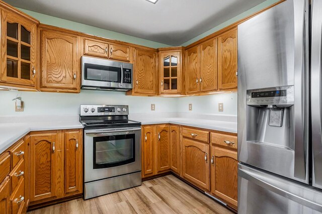 kitchen with glass insert cabinets, brown cabinetry, appliances with stainless steel finishes, and light countertops