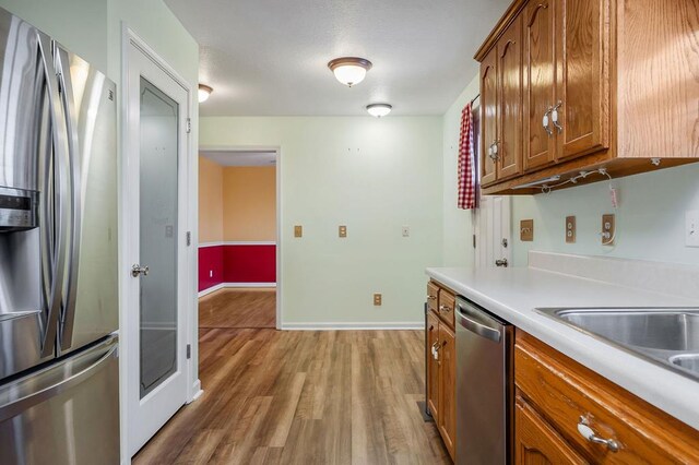 kitchen with stainless steel appliances, baseboards, light countertops, light wood-type flooring, and brown cabinets