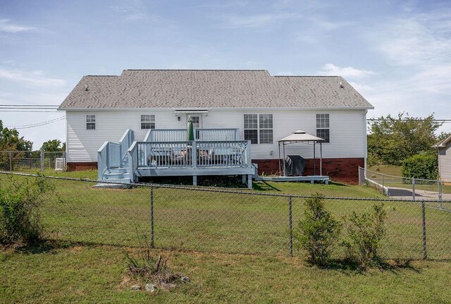 rear view of property featuring a lawn, a fenced backyard, a trampoline, a deck, and a gazebo