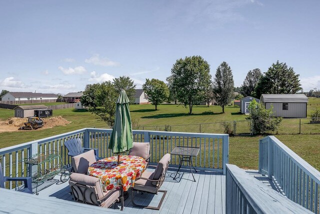 wooden terrace featuring a storage shed, a yard, outdoor dining area, and an outbuilding