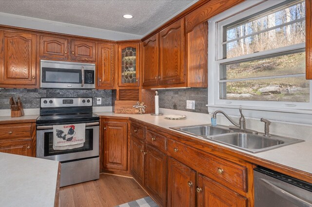 kitchen with brown cabinets, stainless steel appliances, light countertops, glass insert cabinets, and a sink