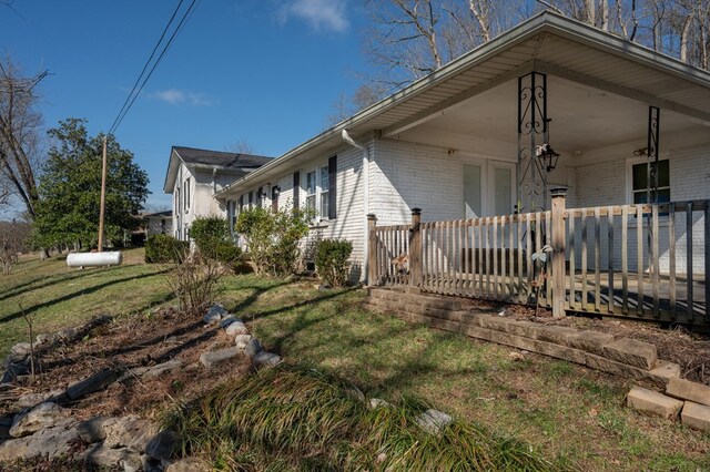 view of property exterior with covered porch, brick siding, and a lawn