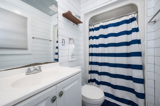 full bath with wooden walls, a shower with shower curtain, vanity, and toilet