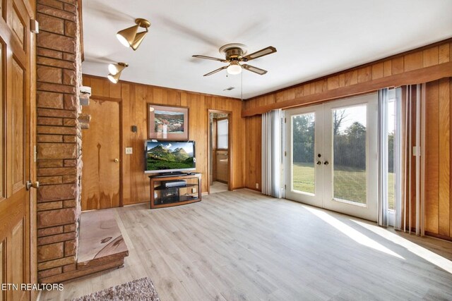 unfurnished living room featuring light wood-type flooring, ceiling fan, wooden walls, and french doors