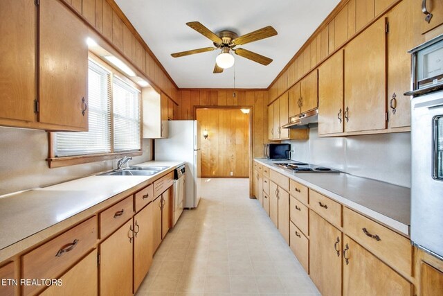 kitchen with light countertops, stainless steel gas stovetop, brown cabinetry, a sink, and under cabinet range hood