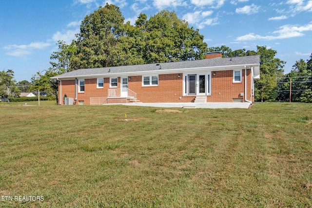 rear view of property with entry steps, brick siding, a lawn, and a chimney