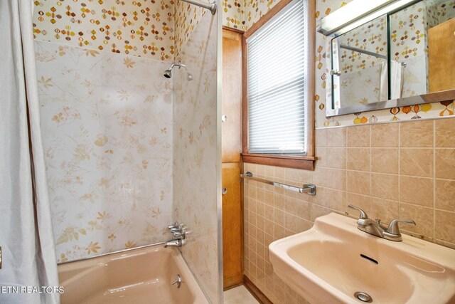 bathroom featuring tile walls, shower / bath combo with shower curtain, and a sink