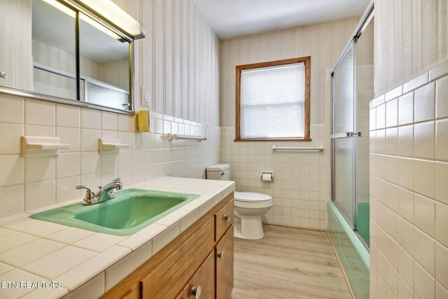 full bath featuring toilet, enclosed tub / shower combo, vanity, wood finished floors, and wallpapered walls